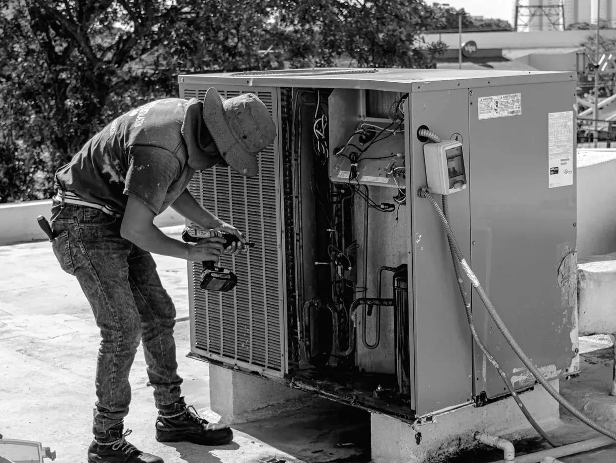 An HVAC technician bent into the side of a rooftop condensing unit.